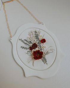 a white plate with red flowers on it hanging from a gold - toned chain