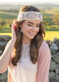 a woman with long hair wearing a headband and smiling at the camera while standing in front of a stone wall