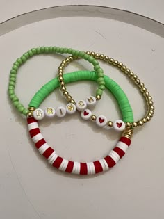 Get festive with this trendy and stretchy Christmas Grinch theme 3 piece stackable bundle with gold lettering.  This set makes the perfect gift for a friend or for yourself!  This set is made with non tarnish gold beads.  *If you are unsure if a bracelet will fit you, follow these steps: -  measure your wrist with a flexible measuring tape, ribbon or strip of paper. - If you used a ribbon or strip of paper make a mark where the ends would meet. Lay it flat and use a ruler   to measure the length. That number will be your wrist measurement. - if you would like a snug fit, add about 1/4" -if you would like a bit more comfort then add about 1/2" *This particular set of bracelets is 7 inches **If you would like this bracelet set in a different size, please free to message me and I'll do my bes Cute Clay Bead Bracelet Ideas Christmas, Christmas Bracelet Ideas Seed Beads, Flat Bead Ideas, Christmas Bracelet Ideas Glass Beads, Grinch Bracelet Ideas, Preppy Christmas Bracelets, Christmas Braclets Ideas, Christmas Bead Bracelets, Christmas Bracelets Beaded