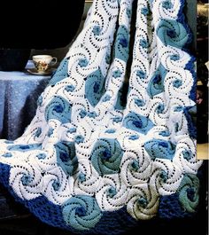 a blue and white crocheted blanket sitting on top of a chair next to a table