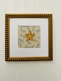 a gold framed starfish is hanging on the wall