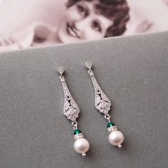 a pair of earrings with pearls and green stones on top of a table next to a magazine