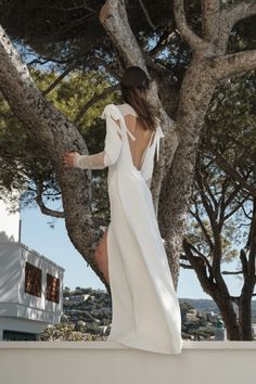 a woman in a white dress is standing on a ledge near some trees and looking at the sky