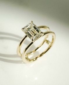 an engagement ring with a princess cut diamond set in yellow gold, on a white surface