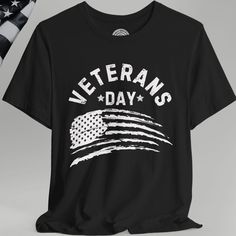 Honor our heroes in style with this American Veteran Crew Neck T-shirt featuring a bold, distressed American Flag and the words "Veterans Day" in a rugged, grunge-style block font. This comfortable, high-quality tee is perfect for showing your patriotic pride and supporting veterans on Veterans Day or any occasion. Whether you're attending an event, parade, or simply looking for a meaningful gift for the veterans in your life, this shirt is a must-have for any proud American. Product Details This classic unisex jersey short sleeve tee fits like a well-loved favorite. Soft cotton and quality print make users fall in love with it over and over again. These t-shirts have-ribbed knit collars to bolster shaping. The shoulders are tapered for a better fit over time. Dual side seams hold the garm Patriotic Black T-shirt For Veterans Day, Memorial Day Streetwear T-shirt With Letter Print, Black Patriotic T-shirt With Letter Print, Black T-shirt With Graphic Print For Veterans Day, Letter Print Tops For Streetwear, Black Graphic Print T-shirt For Memorial Day, Bike Rally, Distressed American Flag, Proud American