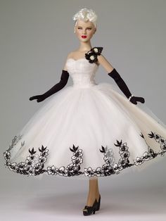 a barbie doll wearing a white dress with black gloves and flowers on it's head