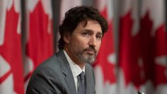 a man in a suit and tie standing at a podium with canadian flags behind him