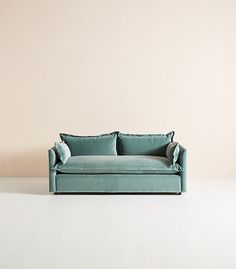 a blue couch sitting on top of a white floor next to a wall with a light pink background