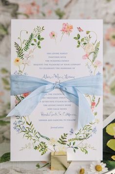 the wedding stationery is adorned with blue ribbon and flowers, which are tied together