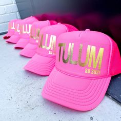 three pink hats with gold lettering on them sitting next to each other in front of a brick wall