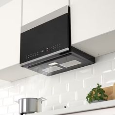 a kitchen with white cabinets and stainless steel range hood over the stove, in front of a potted plant