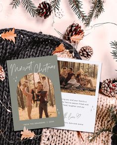 two christmas cards on top of a knitted blanket next to pine cones and fir trees