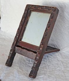 an old wooden stand with a mirror on it's legs, sitting on a white sheet