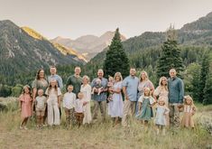 a large group of people standing on top of a grass covered field in front of mountains