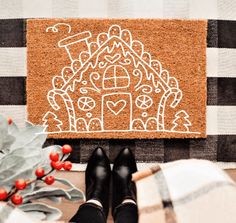 a person standing in front of a door mat with a gingerbread house drawn on it