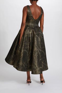 a woman wearing a black and gold dress with an intricate print on the skirt, back view