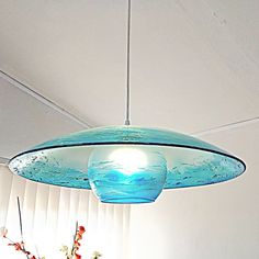 a blue glass light hanging from the ceiling in a room with white walls and windows