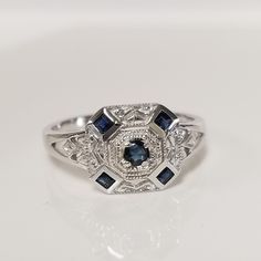 a white gold ring with blue sapphires and diamonds in the center on a white surface