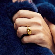 a woman's hand with a gold ring on her left wrist, wearing a blue fur coat