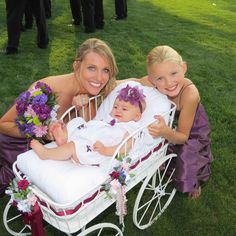 two women and a baby in a white carriage with flowers on the side, posing for a photo