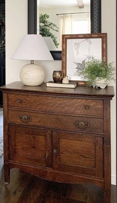 a wooden dresser with a lamp on top of it and a mirror in the background