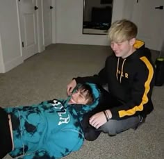 two young boys sitting on the floor playing with each other and one boy wearing a hoodie