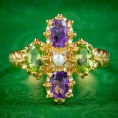 A striking Suffragette style ring claw set with two violet amethysts, two green peridots (approx. 0.45ct each) and a central white pearl. Together, the colours of each stone pay tribute to the women's Suffragette movement and symbolise; Violet for Loyalty, White for Purity and Green for Hope, or Give Women Votes!  The ring is fashioned in gold gilded silver and displays beautiful engraving across the gallery and shoulders. It boasts a colourful collection of gemstones and looks lovely crowning t Green Amethyst Ring For Formal Occasions, Antique Green Multi-stone Ring, Green Amethyst Ring Fine Jewelry, Green Amethyst Rings In Fine Jewelry Style, Wedding Amethyst Ring With Green Center Stone, Green Amethyst Ring With Center Stone For Wedding, Green Amethyst Birthstone Ring In Fine Jewelry Style, Green Amethyst Ring For Anniversary, May Birthstone, Green Amethyst Birthstone Ring