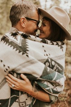 a man and woman wrapped up in blankets are smiling at each other as they walk through the woods