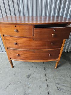 a wooden dresser with two drawers and three knobs on the top, in front of a corrugated wall