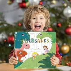 a young boy is holding up a dinosaur puzzle board in front of a christmas tree