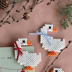 two cross stitch sheep ornament hanging on a tree branch with pine cones in the background