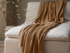 a white couch with a blanket on top of it next to a vase with flowers