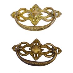 two antique brass drawer pulls, one has an ornate design and the other has a decorative handle