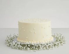 a cake with white frosting and small flowers on the top is sitting on a table