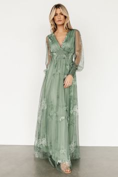 a woman wearing a long green dress with sheer sleeves and flowers on the front,