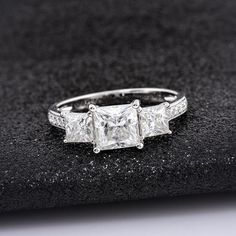 three stone princess cut diamond ring with side stones in white gold or silver, on a black velvet surface