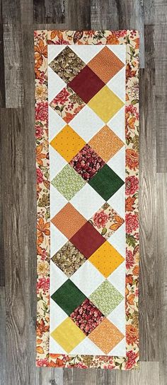 an orange, yellow and green patchwork quilt hanging on a wooden wall next to a wood floor