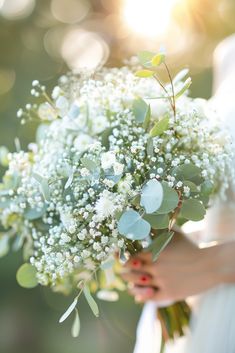 a bridal holding a bouquet of white flowers and greenery in her left hand