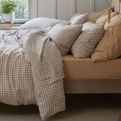 an unmade bed with pillows and blankets in front of a window, next to a potted plant