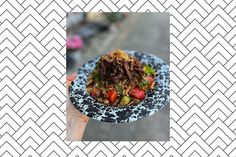 a hand holding a black and white plate with food on it