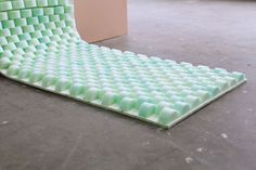 a green and white sculpture sitting on top of a cement floor next to a wall