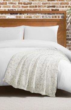 a bed with white sheets and pillows in front of a brick wall