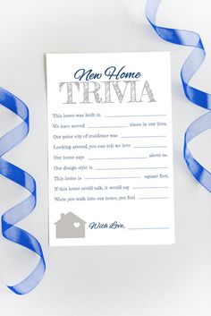 a new home trivia card with blue ribbon on white paper next to streamers