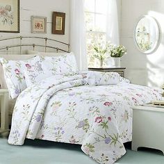 a white bed with flowers on it next to a dresser and window in a room