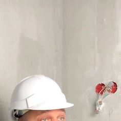 a man wearing a hard hat standing next to a wall with a screwdriver on it