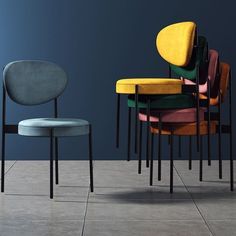 four chairs with different colors and shapes in front of a dark blue wall on the floor