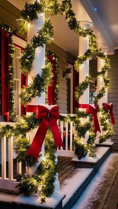 christmas wreaths on the front porch decorated with red bows and white pillar lights are adorned with greenery