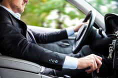 a man in a suit driving a car with his hand on the steering wheel and wearing a keychain