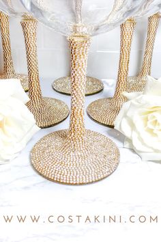 two champagne flutes are sitting on a table with white roses and glass vases in the background