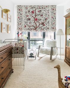 a baby's room with a rocking chair, crib and window covered in wallpaper